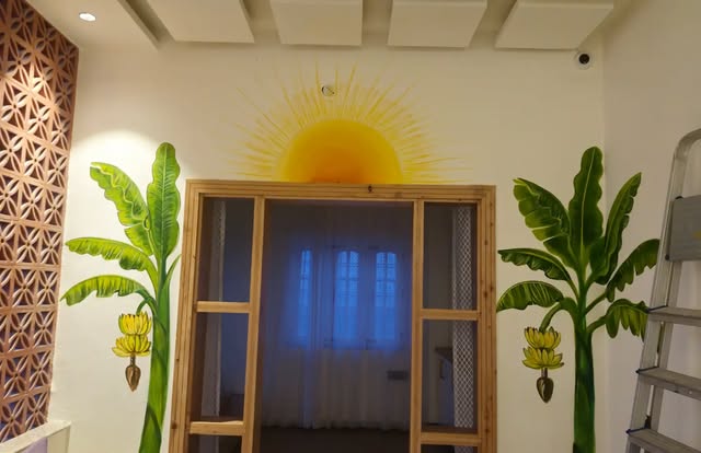 Room with a golden sun painted around the window and banana trees on both sides